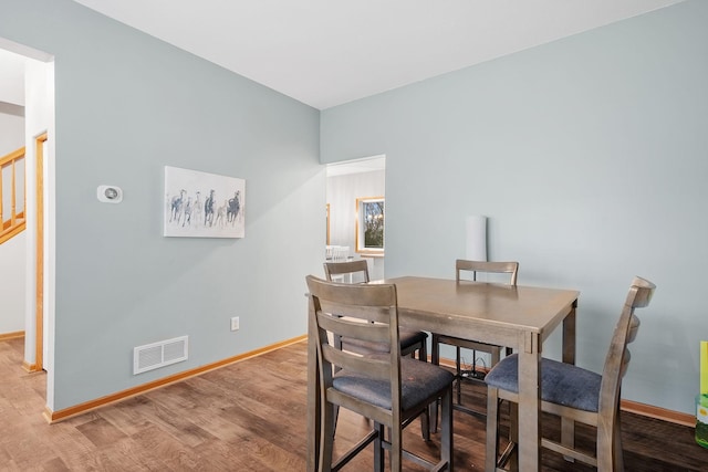dining space featuring stairs, baseboards, visible vents, and wood finished floors