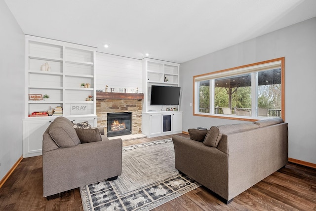 living area featuring baseboards, dark wood-style floors, and a stone fireplace
