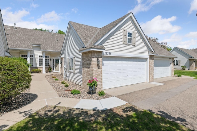 view of front of house featuring roof with shingles, brick siding, and driveway