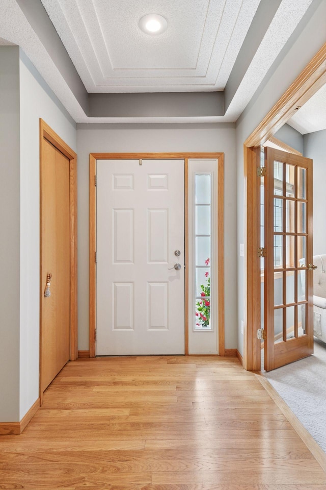 foyer with a tray ceiling, light wood-type flooring, and baseboards
