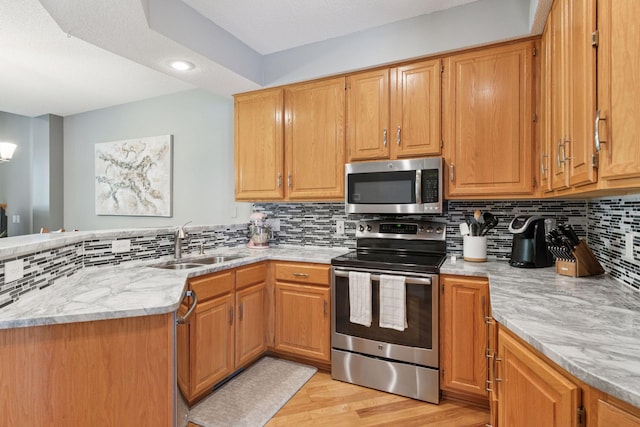 kitchen with stainless steel appliances, a sink, light wood-style floors, a peninsula, and decorative backsplash