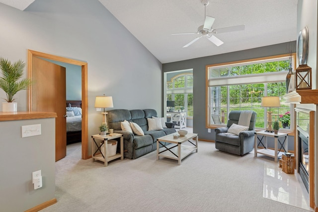 carpeted living area with a glass covered fireplace, ceiling fan, and high vaulted ceiling
