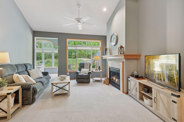 living room featuring lofted ceiling, a fireplace with flush hearth, ceiling fan, and light carpet