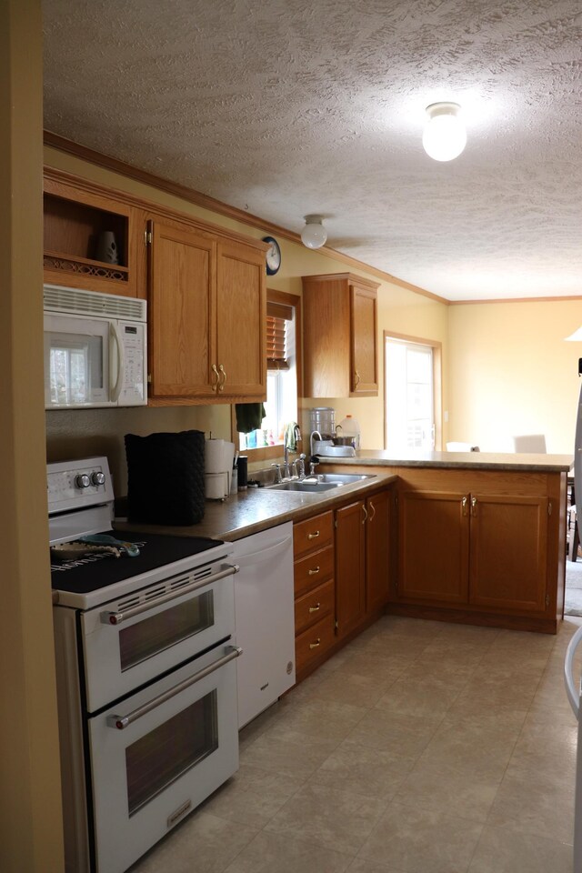 kitchen featuring a sink, white appliances, a textured ceiling, a peninsula, and ornamental molding