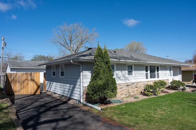view of side of home with a lawn, roof with shingles, and fence