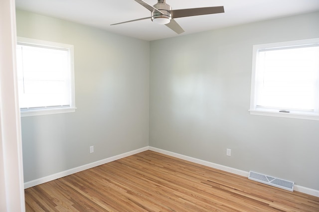 spare room featuring a wealth of natural light, light wood-type flooring, ceiling fan, and visible vents