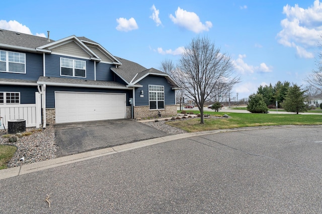 view of front facade featuring roof with shingles, central AC, stone siding, a garage, and aphalt driveway
