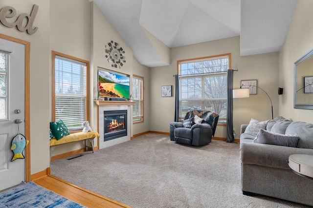 living area with a glass covered fireplace, baseboards, vaulted ceiling, and visible vents