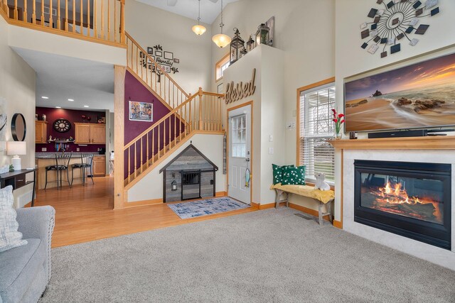 carpeted living room with a high ceiling, a glass covered fireplace, stairs, baseboards, and wood finished floors