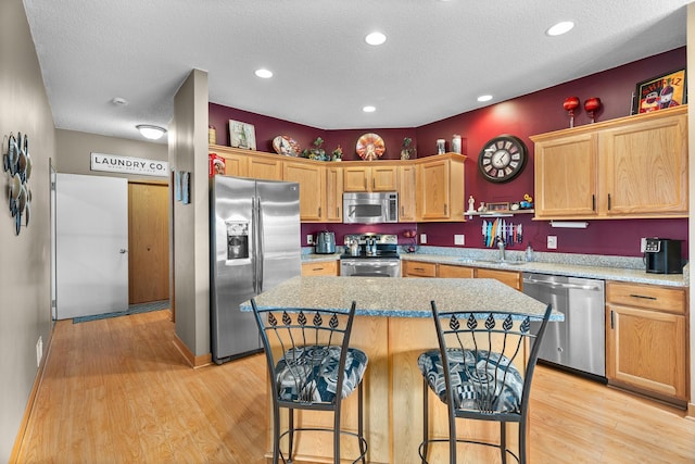 kitchen with light wood-style flooring, a breakfast bar, stainless steel appliances, and a textured ceiling