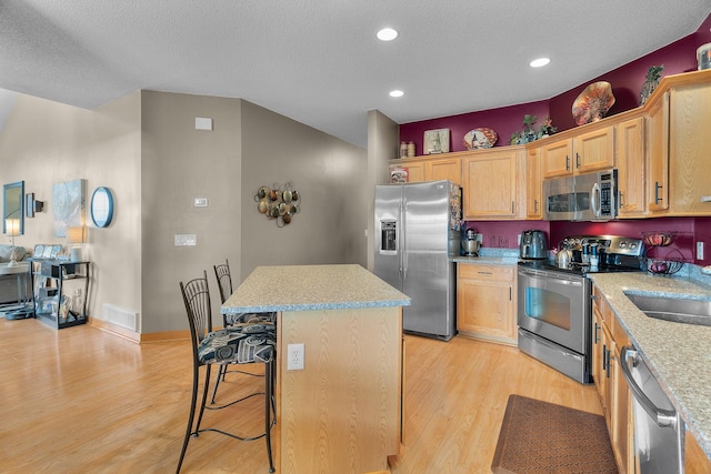 kitchen featuring visible vents, a kitchen island, a breakfast bar area, light wood finished floors, and appliances with stainless steel finishes