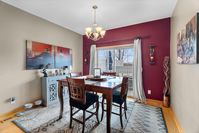 dining space featuring baseboards, a notable chandelier, wood finished floors, and visible vents