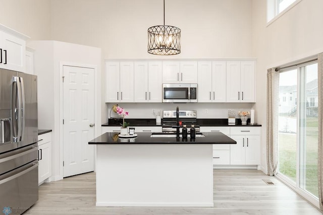 kitchen featuring a towering ceiling, dark countertops, light wood-type flooring, white cabinets, and stainless steel appliances