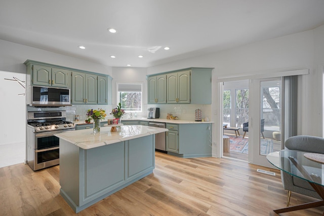 kitchen featuring appliances with stainless steel finishes, green cabinetry, backsplash, and light wood finished floors