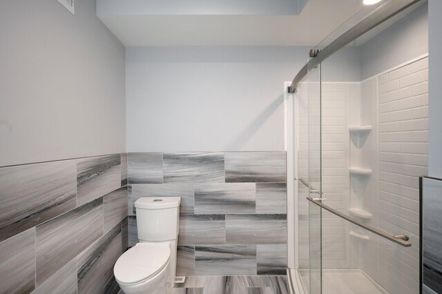 full bathroom with wainscoting, tile walls, a shower stall, and toilet