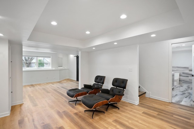 living area featuring light wood-type flooring, baseboards, and a tray ceiling