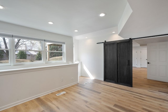 unfurnished room featuring a barn door, light wood finished floors, recessed lighting, baseboards, and visible vents
