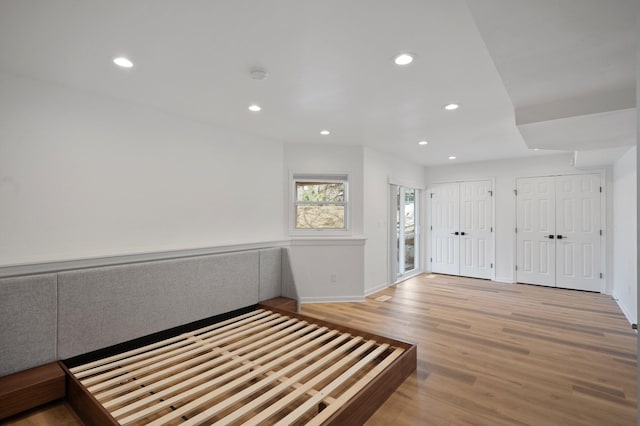 unfurnished bedroom with recessed lighting, multiple closets, light wood finished floors, and baseboards