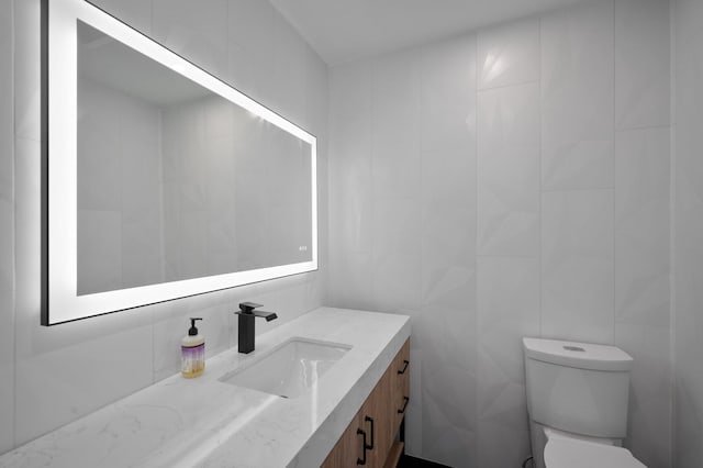 bathroom featuring vanity, toilet, and tile walls