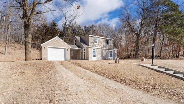 view of front facade with dirt driveway, a garage, and view of wooded area