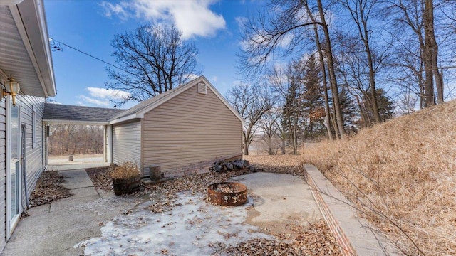 view of side of property featuring an outdoor fire pit, a shingled roof, and a patio area