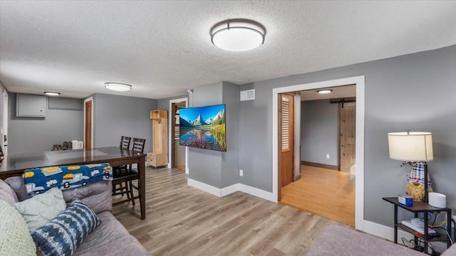 living room with light wood-type flooring, baseboards, and a textured ceiling