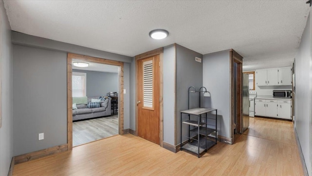 corridor with light wood-type flooring, baseboards, and a textured ceiling