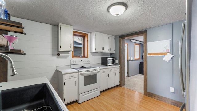 kitchen featuring white range with electric stovetop, a sink, stainless steel microwave, light countertops, and white cabinetry