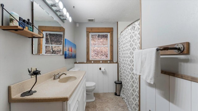 bathroom with toilet, vanity, a wainscoted wall, a textured ceiling, and a shower with shower curtain