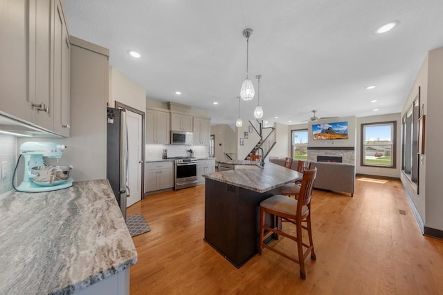 2120 Violet Ln, Faribault, MN 55021 - kitchen featuring ceiling fan, appliances with stainless steel finishes, a warm lit fireplace, light wood-style floors, and a breakfast bar
