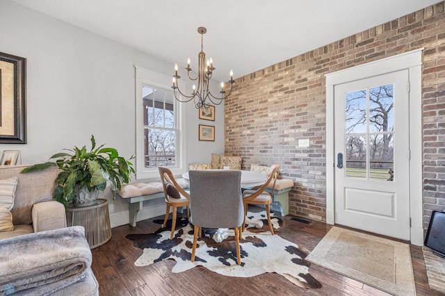 dining space with brick wall, visible vents, baseboards, wood-type flooring, and a notable chandelier