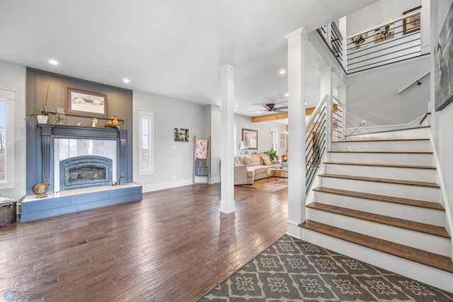 living room featuring a ceiling fan, a high end fireplace, stairway, wood-type flooring, and ornate columns