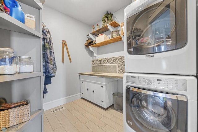 clothes washing area with laundry area, visible vents, stacked washer / dryer, baseboards, and light wood-type flooring