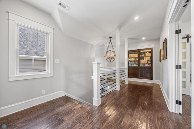 hall with an inviting chandelier, hardwood / wood-style floors, baseboards, an upstairs landing, and visible vents