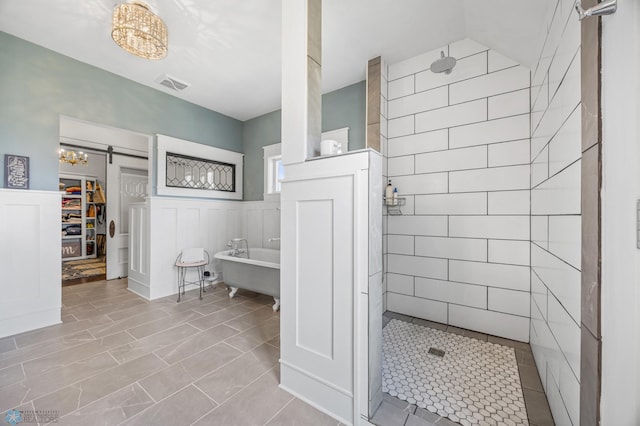 full bath with a notable chandelier, a freestanding bath, a wainscoted wall, visible vents, and tiled shower