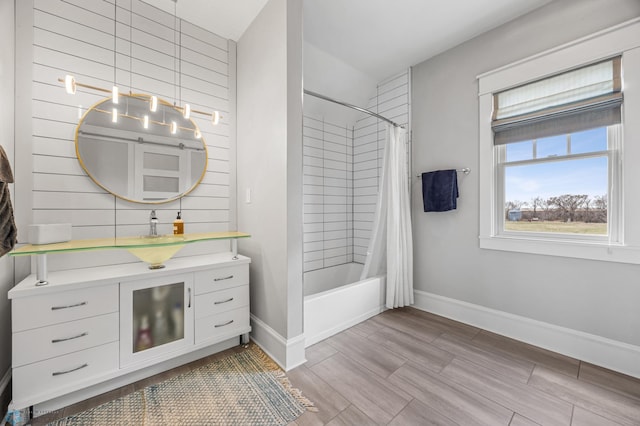 bathroom with baseboards, shower / bathtub combination with curtain, and vanity