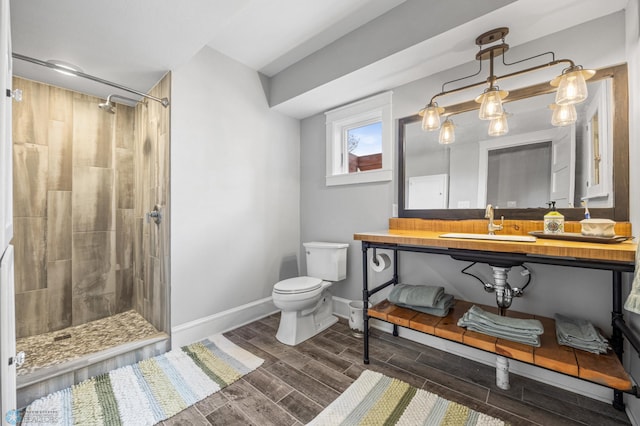 bathroom with toilet, baseboards, tiled shower, and wood finished floors
