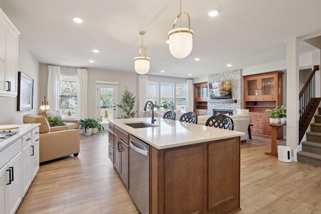 kitchen featuring a stone fireplace, open floor plan, light countertops, a sink, and dishwasher
