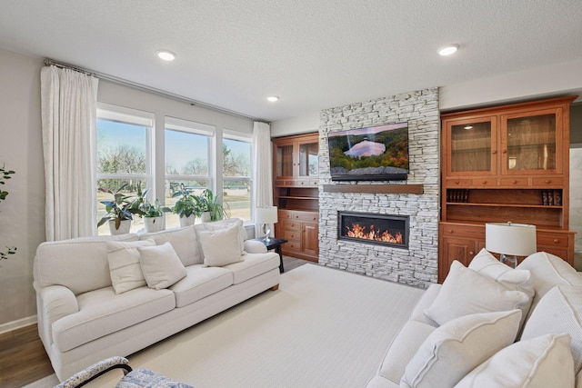 living room with a textured ceiling, a stone fireplace, recessed lighting, baseboards, and wood finished floors