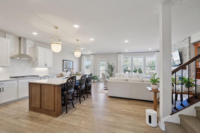 4994 Obsidian Way, Victoria, MN 55386 - kitchen with wall chimney exhaust hood, open floor plan, stainless steel gas cooktop, light countertops, and a breakfast bar area