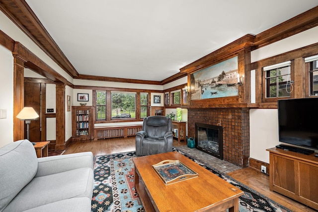 2511 12th Ave N, Minneapolis, MN 55411 - living room featuring radiator heating unit, wood finished floors, crown molding, a brick fireplace, and decorative columns