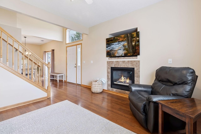 living area with wood finished floors, stairway, a ceiling fan, baseboards, and a tile fireplace