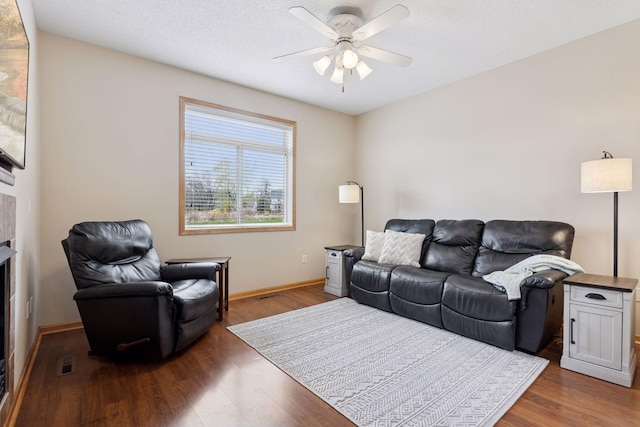 living room featuring baseboards, a fireplace, ceiling fan, and wood finished floors