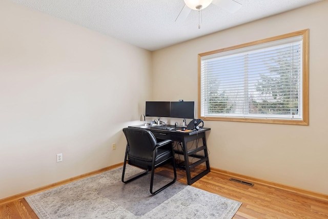 office area with a textured ceiling, baseboards, visible vents, ceiling fan, and wood finished floors