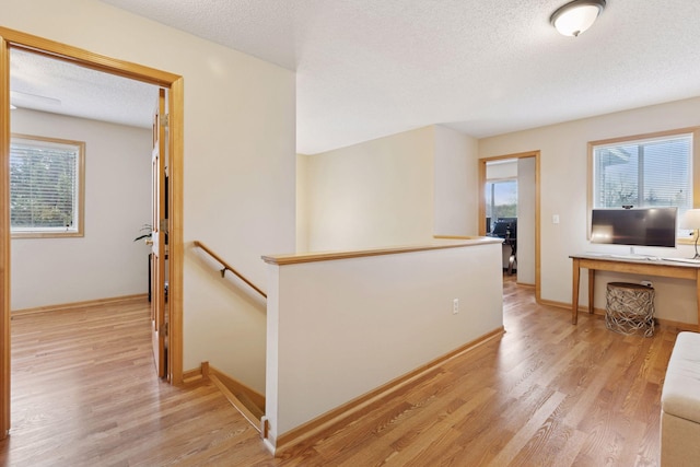 corridor featuring a textured ceiling, an upstairs landing, light wood-style flooring, and a healthy amount of sunlight