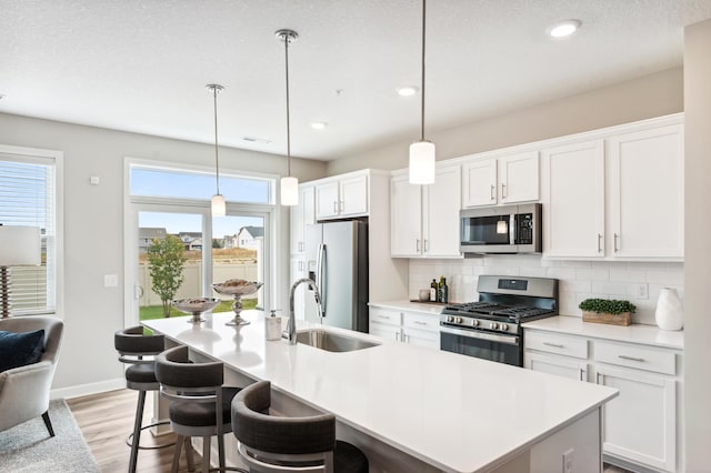 kitchen with decorative backsplash, a kitchen island with sink, light wood-style floors, a sink, and stainless steel appliances