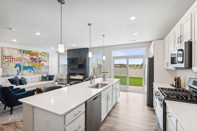 kitchen featuring a sink, light countertops, light wood finished floors, open floor plan, and stainless steel appliances