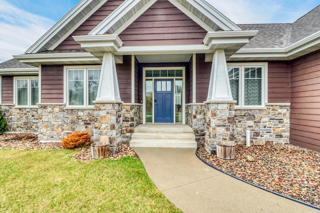 doorway to property with roof with shingles, a lawn, and stone siding