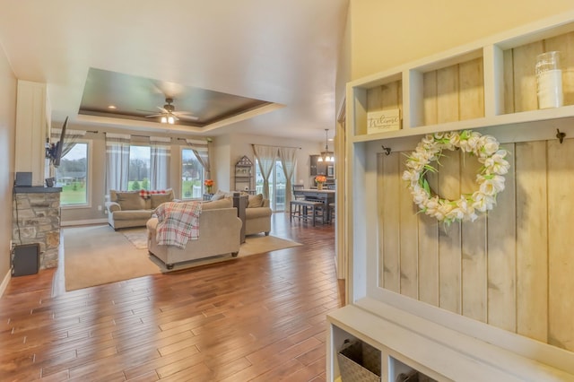 living area with a ceiling fan, baseboards, wood finished floors, and a raised ceiling