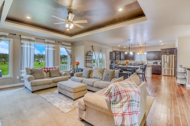 living area featuring recessed lighting, a ceiling fan, light wood finished floors, and a tray ceiling